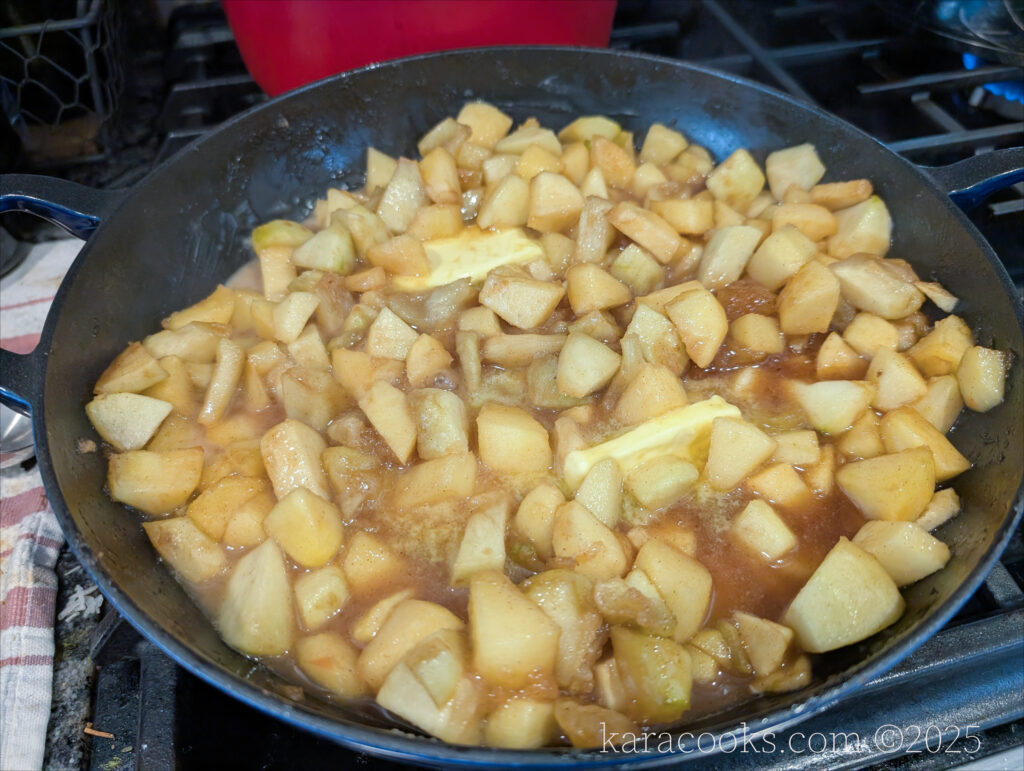 A braiser on the stovetop is full of diced apples, sugar, cinnamon, and nutmeg.