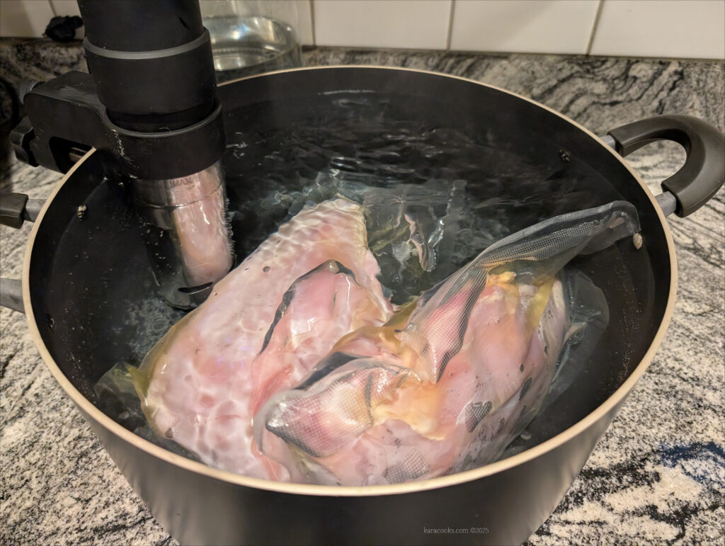 2 bags of turkey breasts are in a large pot with a sous-vide circulator clipped to the side.