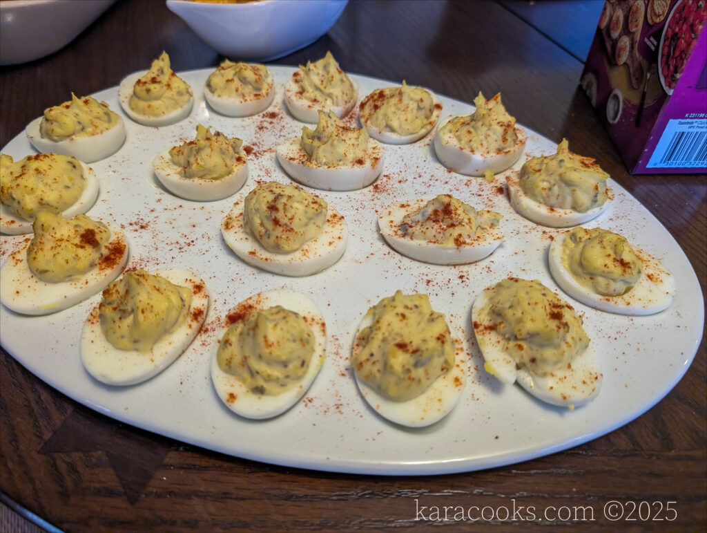 A dozen deviled eggs are displayed in an oval deviled-egg platter. They are sprinkled with dark paprika.
