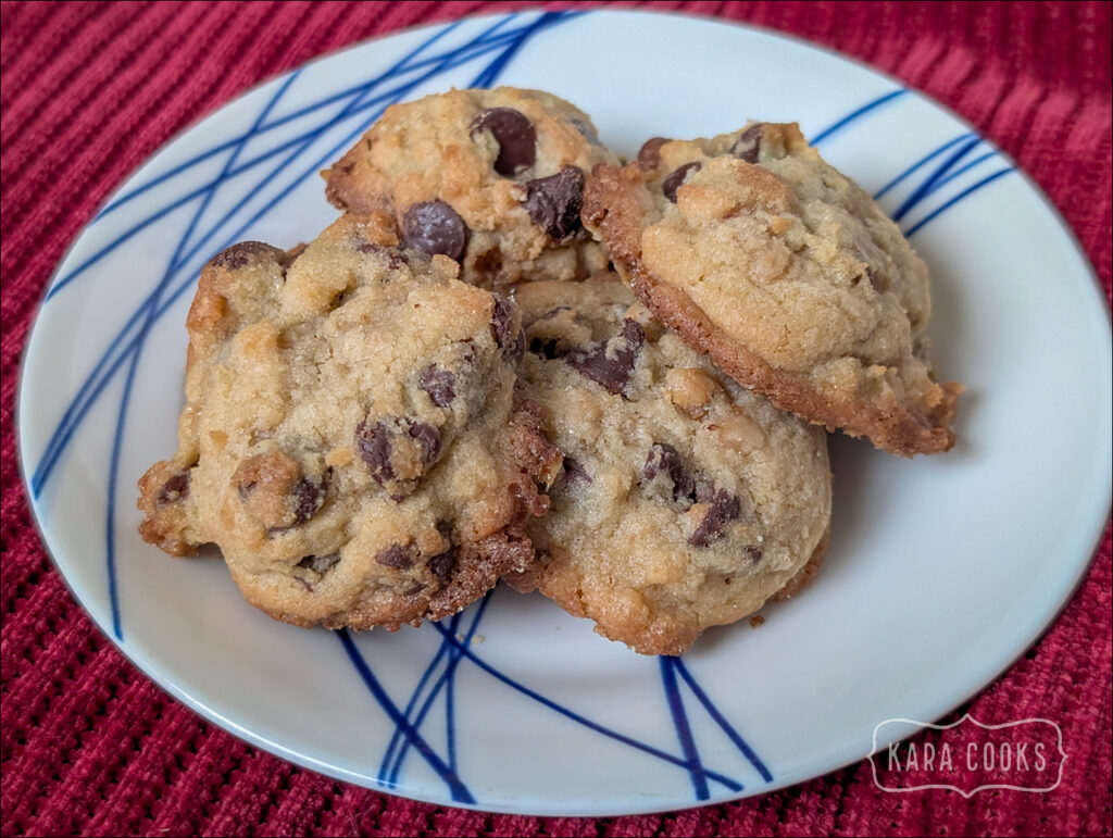 a pile of chocolate chip cookies on a white plate with a blue design on it. The plate is sitting on a red tablecloth.
