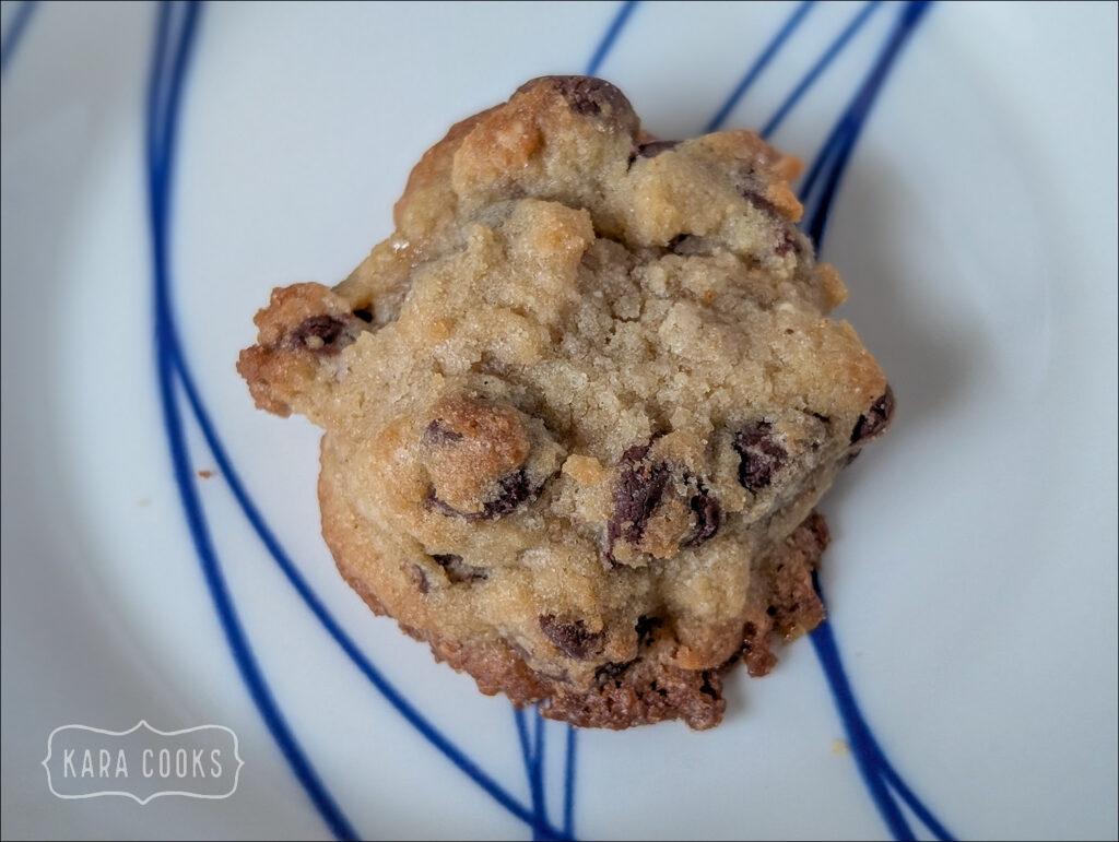 a single chocolate chip cookie on a white plate with a blue design.