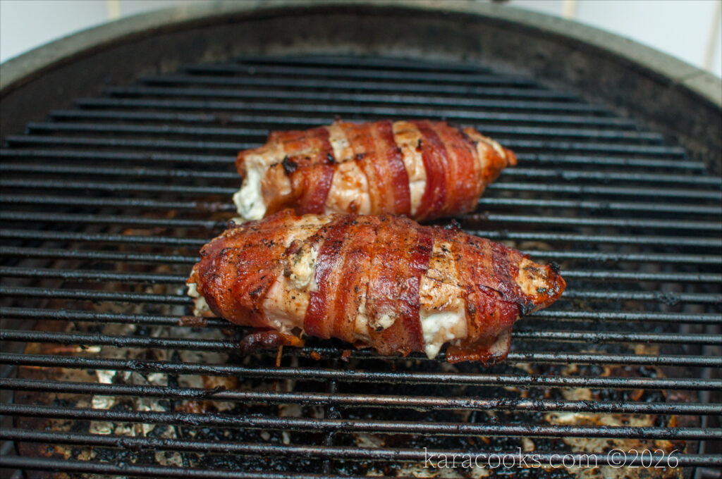 two cooked chicken breasts wrapped in bacon on a kamado grill
