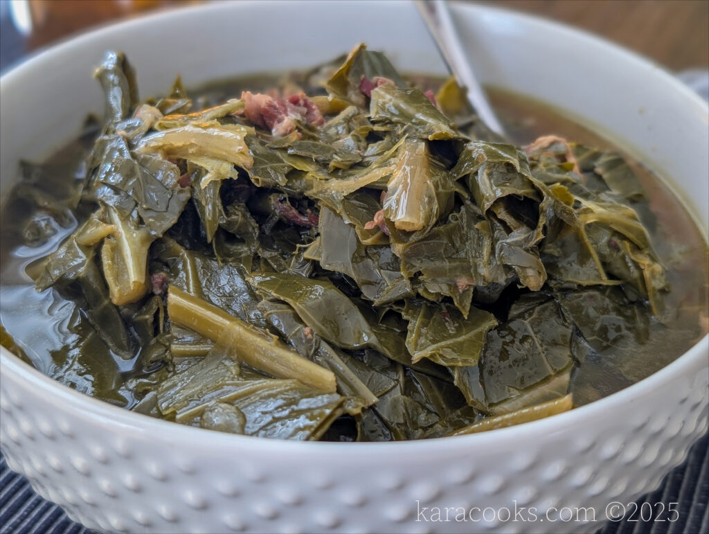 A close up of a white hobnailed bowl full of deep green braised collard greens.